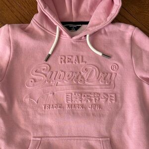 pink Superdry hoodie with an embossed (raised) logo design.